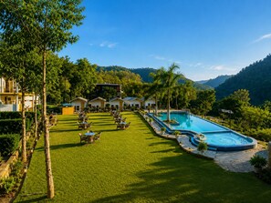 A resort with a swimming pool, outdoor seating, and a view of the surrounding hills. - Wild Vista Marchula Riverside Resort Jim Corbett (Marchula)