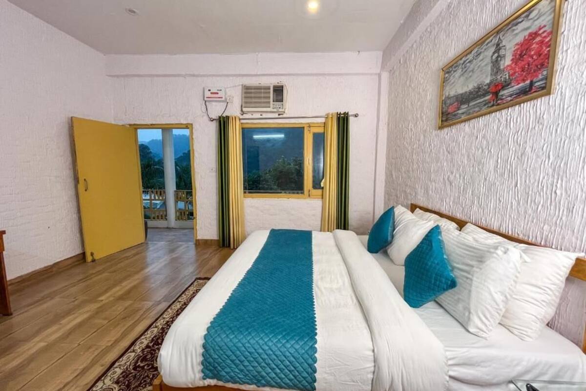 A hotel room with a bed, a window with curtains, an air conditioning unit, and a painting on the wall.