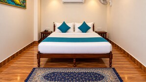 A hotel room with a bed, a nightstand, an air conditioning unit, a wall-mounted fan, and a painting on the wall. - Wild Vista Marchula Riverside Resort Jim Corbett (Marchula)