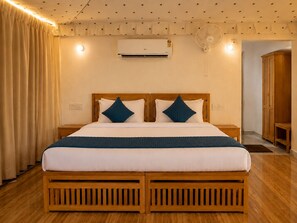 A double bed with a wooden frame, two pillows, a bedside table, an air conditioning unit, a wall-mounted fan, and a wooden wardrobe. - Wild Vista Marchula Riverside Resort Jim Corbett (Marchula)