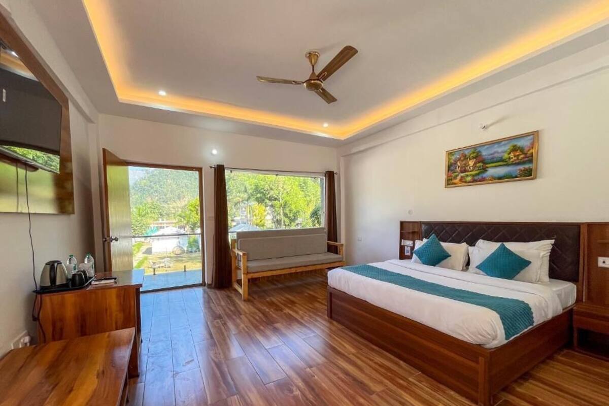 A bedroom with a wooden floor, a bed with white and teal bedding, a ceiling fan, and a painting on the wall.