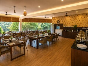 A restaurant with multiple dining tables, chairs, and a kitchen area. - Wild Vista Marchula Riverside Resort Jim Corbett (Marchula)