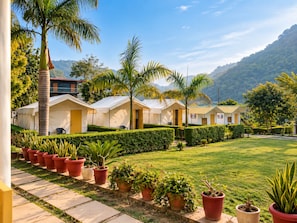 A row of single-story, white-roofed cabins with a well-maintained lawn and potted plants in front. - Wild Vista Marchula Riverside Resort Jim Corbett (Marchula)