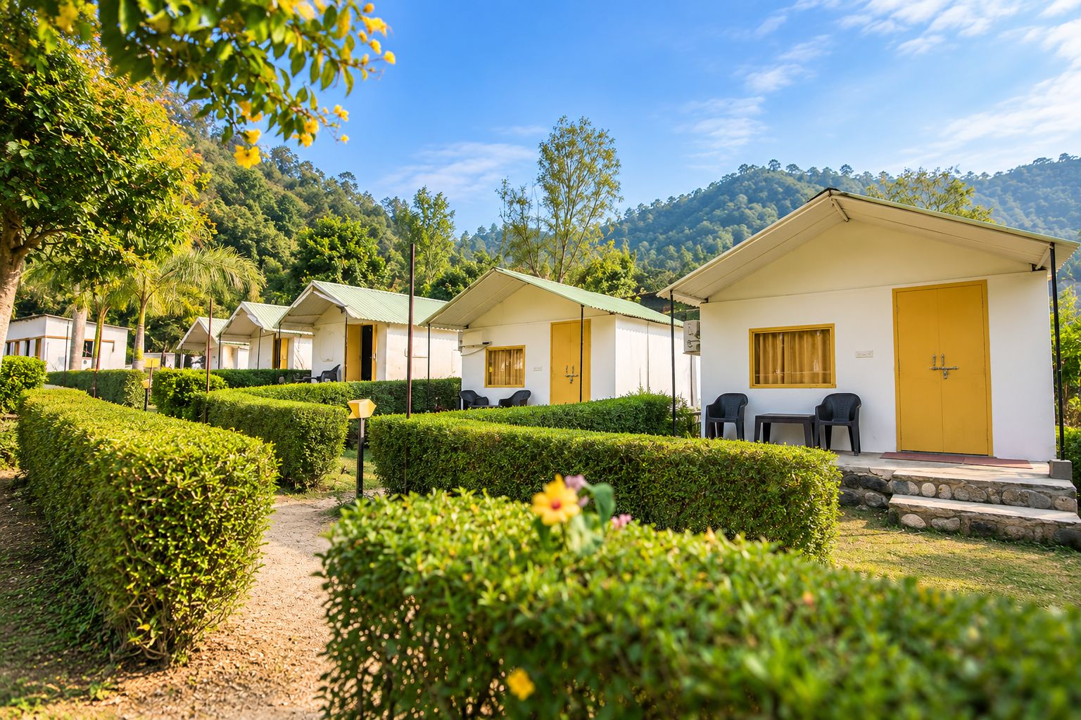 A row of single-story cottages with a paved pathway leading to them, surrounded by well-maintained hedges and a mountainous backdrop.