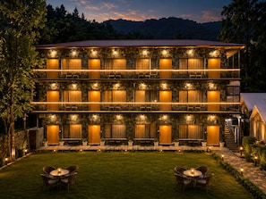 A multi-story hotel with stone facade, multiple balconies, and outdoor seating areas. - Wild Vista Marchula Riverside Resort Jim Corbett (Marchula)