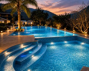 A swimming pool with tiled steps, surrounded by palm trees and a mountain backdrop. - Wild Vista Marchula Riverside Resort Jim Corbett (Marchula)