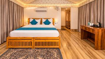 A double bed with a wooden frame, a headboard with two blue pillows, a bedside table with a kettle, and a patterned rug.