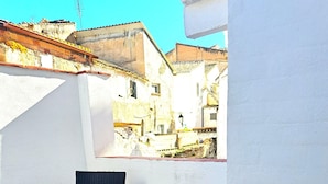A patio with a table and chairs, a white wall, and a view of buildings. - Casa cubo (Alhama de Granada)