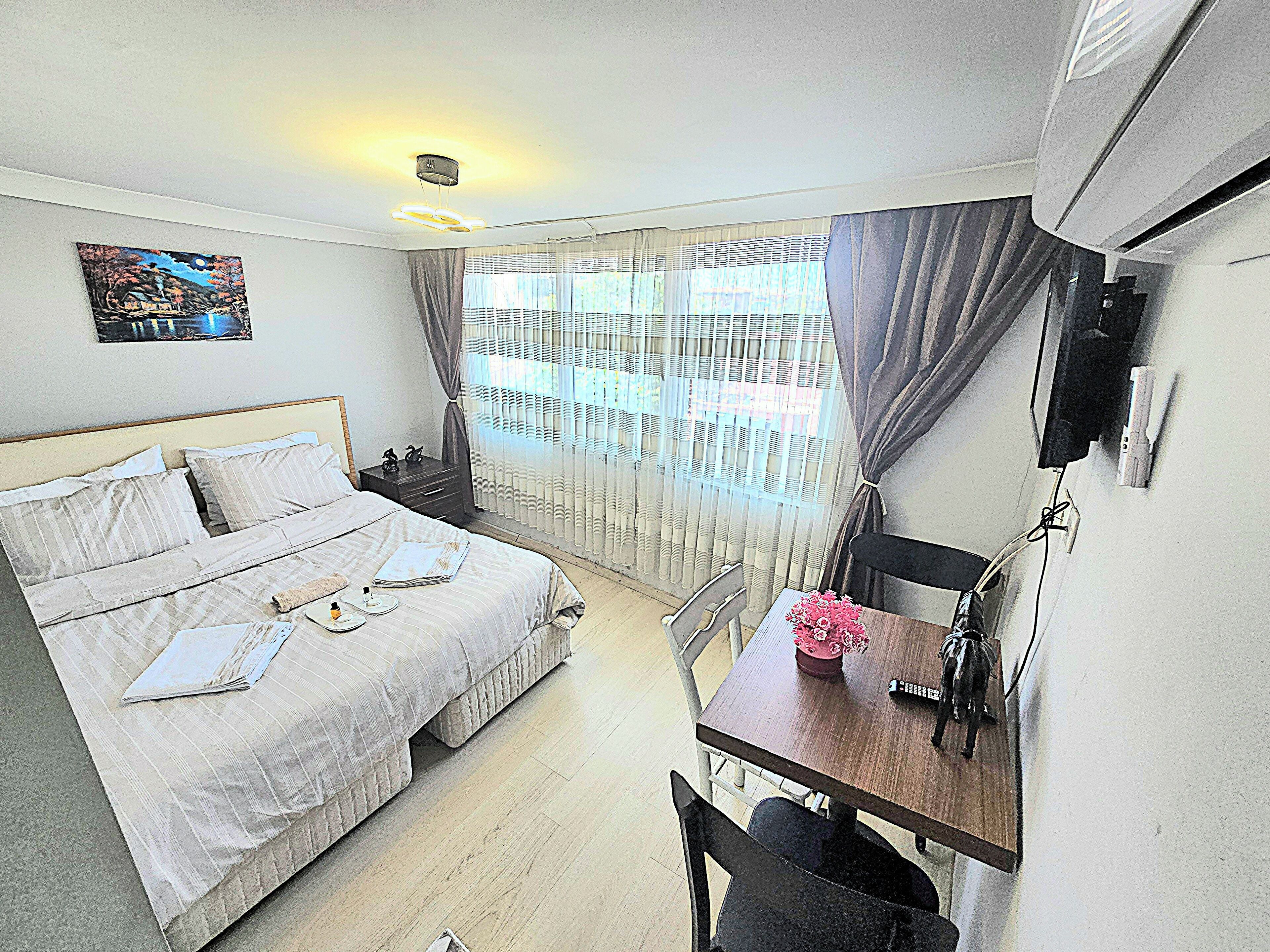 A hotel room with a bed, bedside table, desk, chair, and a painting on the wall.