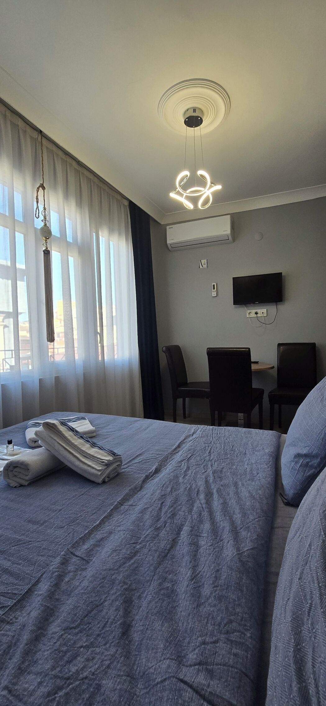 Habitación de hotel con cama, escritorio y una silla. Hay un televisor en la pared y un equipo de aire acondicionado.