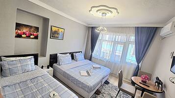 Habitación de hotel con dos camas, una mesita, una silla y un ventanal con cortinas.