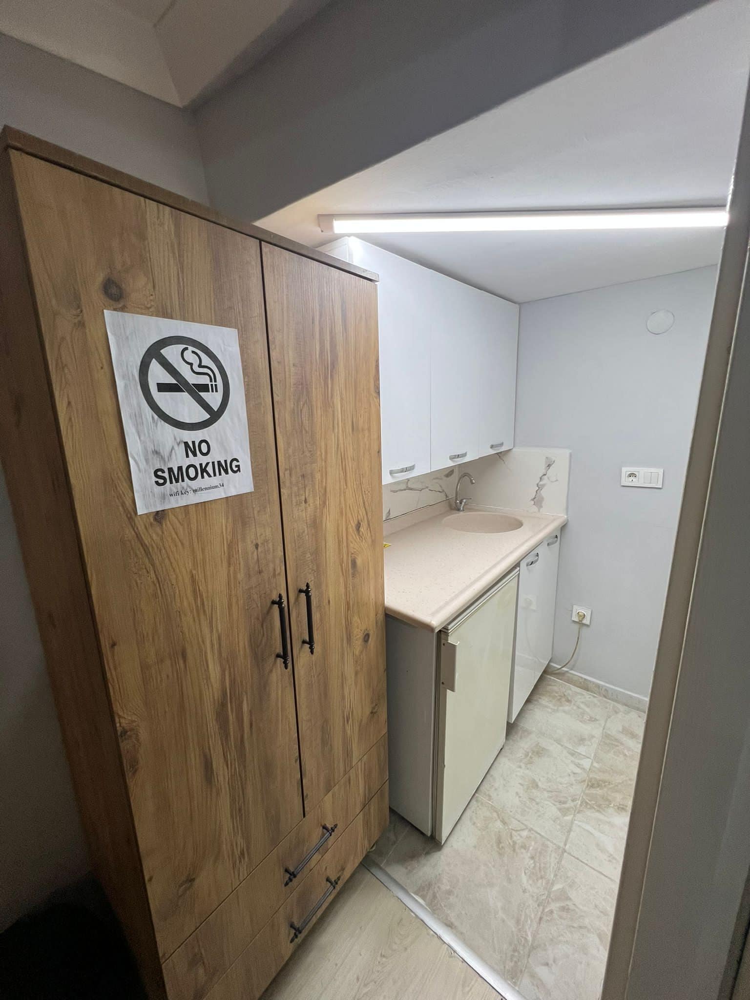 Et badeværelse med et træskab, en håndvask og et skilt med 'No Smoking'.