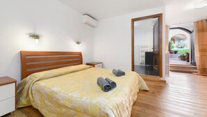 A bedroom with a wooden bed, a nightstand, a wall-mounted air conditioner, and a view of an outdoor patio. - Apartment 'Luna' with Shared Terrace, Wi-Fi and Air Conditioning (San Felice del Benaco)