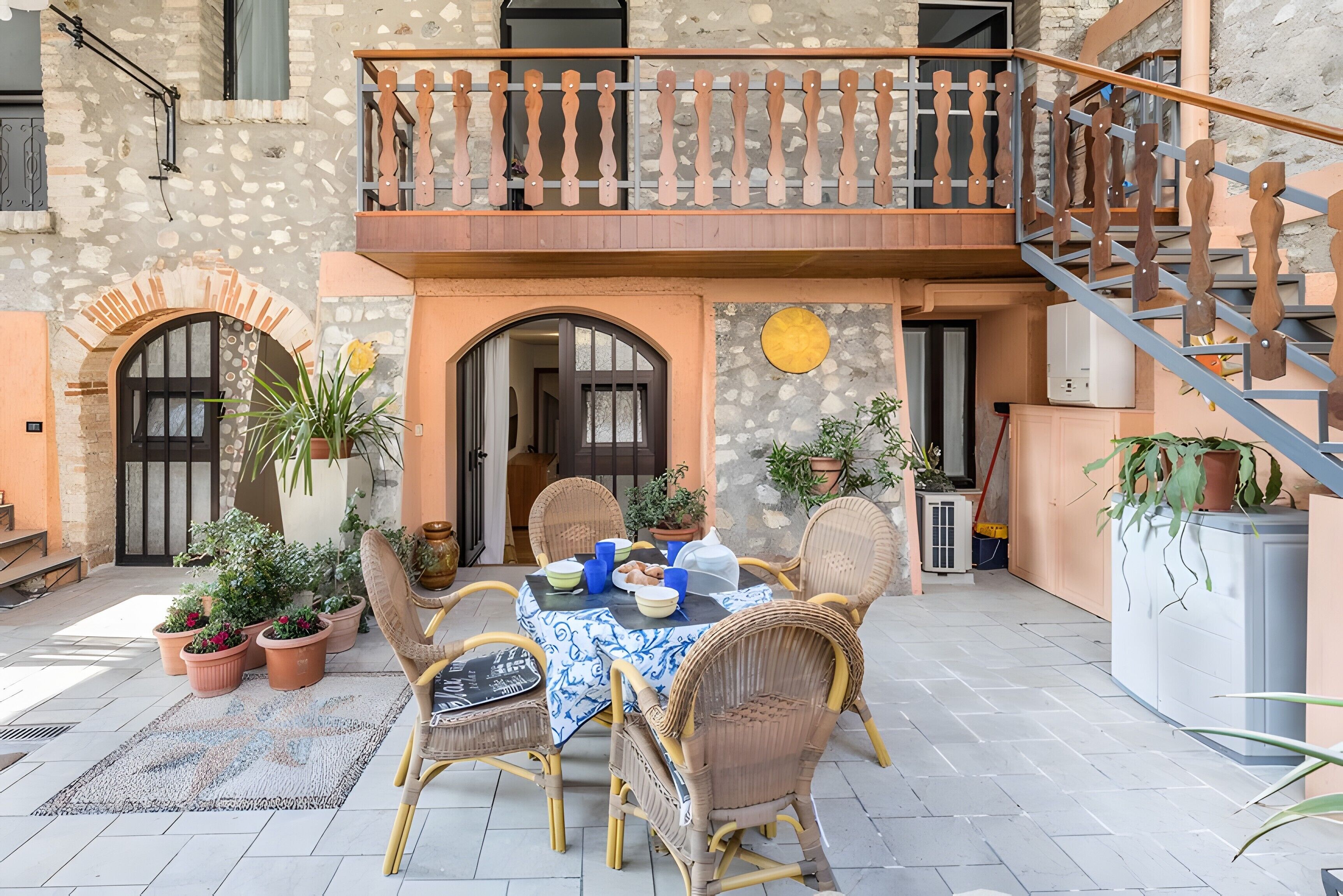 A courtyard with a dining table, chairs, potted plants, and a staircase.
