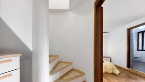 A staircase with wooden steps and white walls, leading to a bedroom with a bed and a bathroom visible through an open door. - Apartment 'Luna' with Shared Terrace, Wi-Fi and Air Conditioning (San Felice del Benaco)