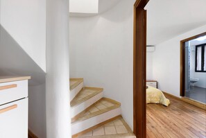 Eine Treppe mit Holzstufen und weißen Wänden führt zu einem Schlafzimmer, durch eine offene Tür ist ein Badezimmer zu sehen.