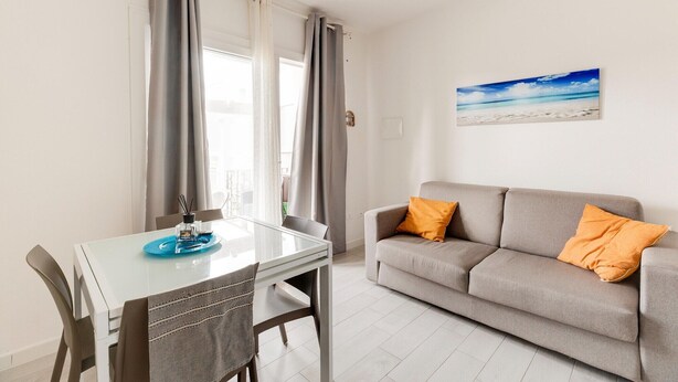 Ein modernes Wohnzimmer mit einem Glastisch, einem grauen Sofa und einem Wandbild im Strandhausstil.
