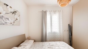 Ein Schlafzimmer mit einem Bett, einer Wandkunst, einem gemusterten Vorhang und einer Deckenleuchte.