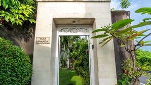 A villa entrance with a sign reading "Villa Ananda," a paved pathway leading to a lush garden, and a stone wall on the right. - Private Pool | Daily Housekeeping | Central Seminyak (Seminyak)