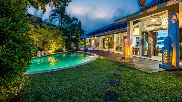 A poolside area with a lounge chair, a wooden deck, and a building with large windows and a covered patio. - Private Pool | Daily Housekeeping | Central Seminyak (Seminyak)