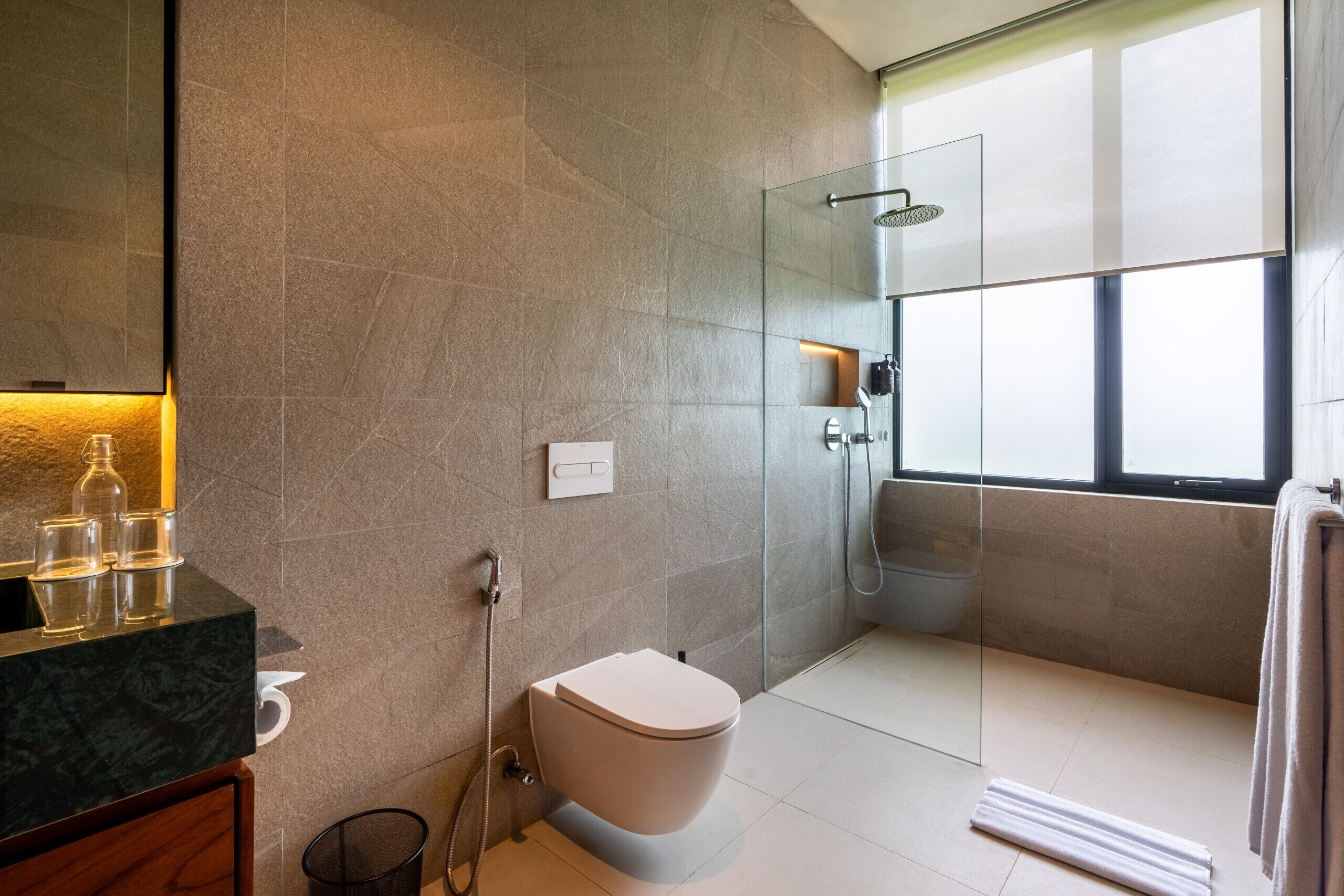 A modern bathroom with a toilet, shower, and large window.