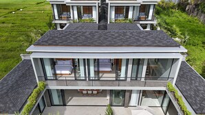 Una casa moderna de dos pisos con un balcón grande, piscina y abundante vegetación.