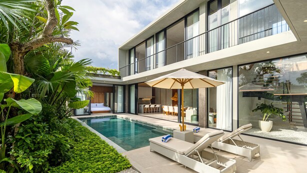 Una casa moderna con piscina, mobiliario exterior y abundante vegetación.