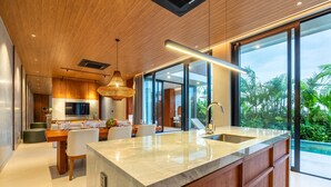 A modern kitchen with a large island, wooden ceiling, and large windows overlooking a garden. - Modern Villa | Private Pool | Near Canggu Beach (Kerobokan)