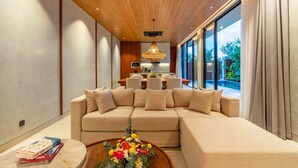 Ein modernes Wohnzimmer mit einem Ecksofa, einem Couchtisch mit floraler Dekoration und einem Essbereich im Hintergrund.