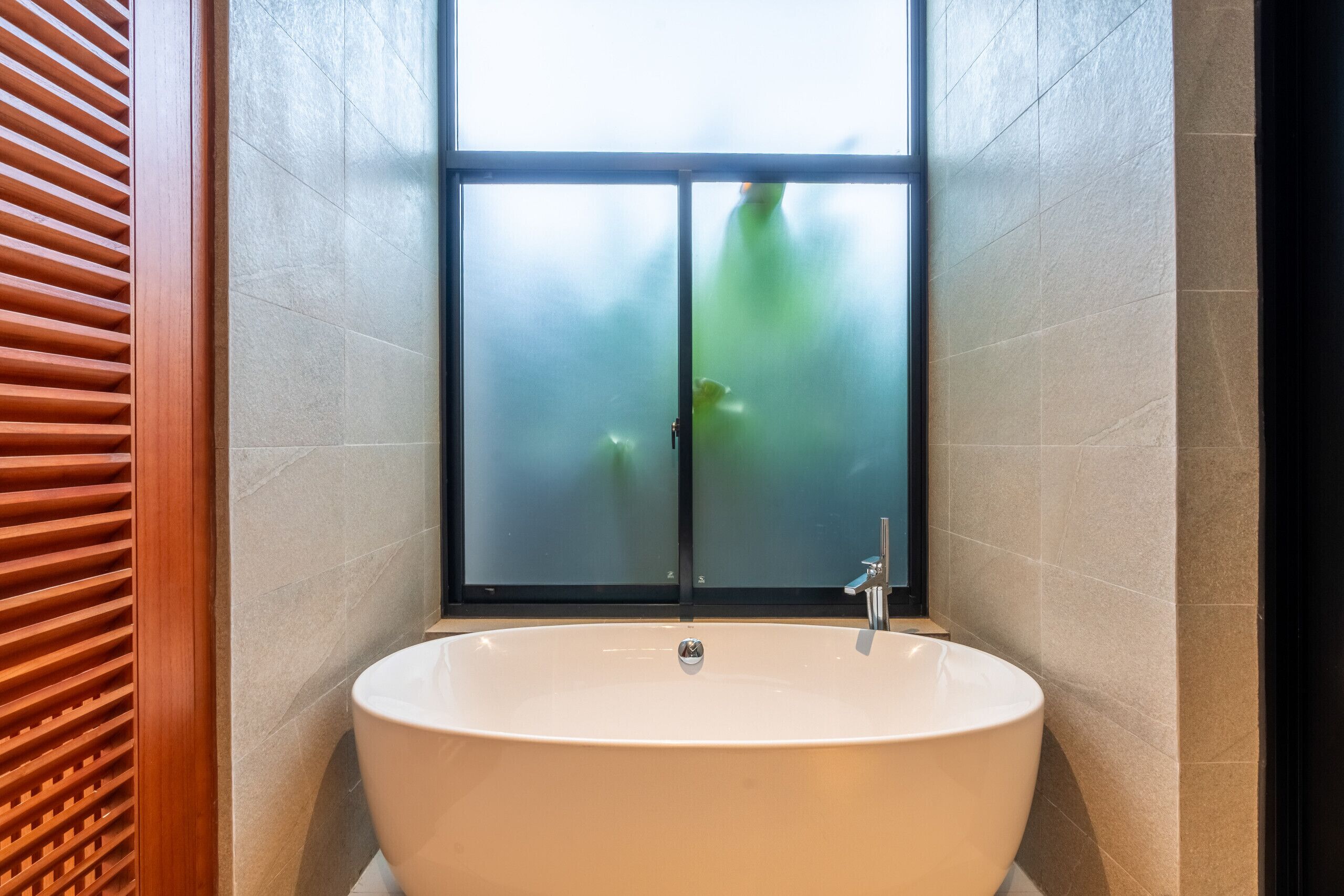 Une salle de bain moderne avec une baignoire îlot, des portes en verre dépoli et un mur avec des lambris en bois.