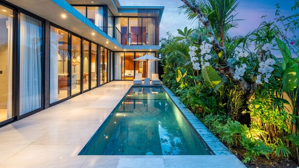 Ein modernes Haus mit Schwimmbad, großen Glasfenstern und üppiger Bepflanzung.