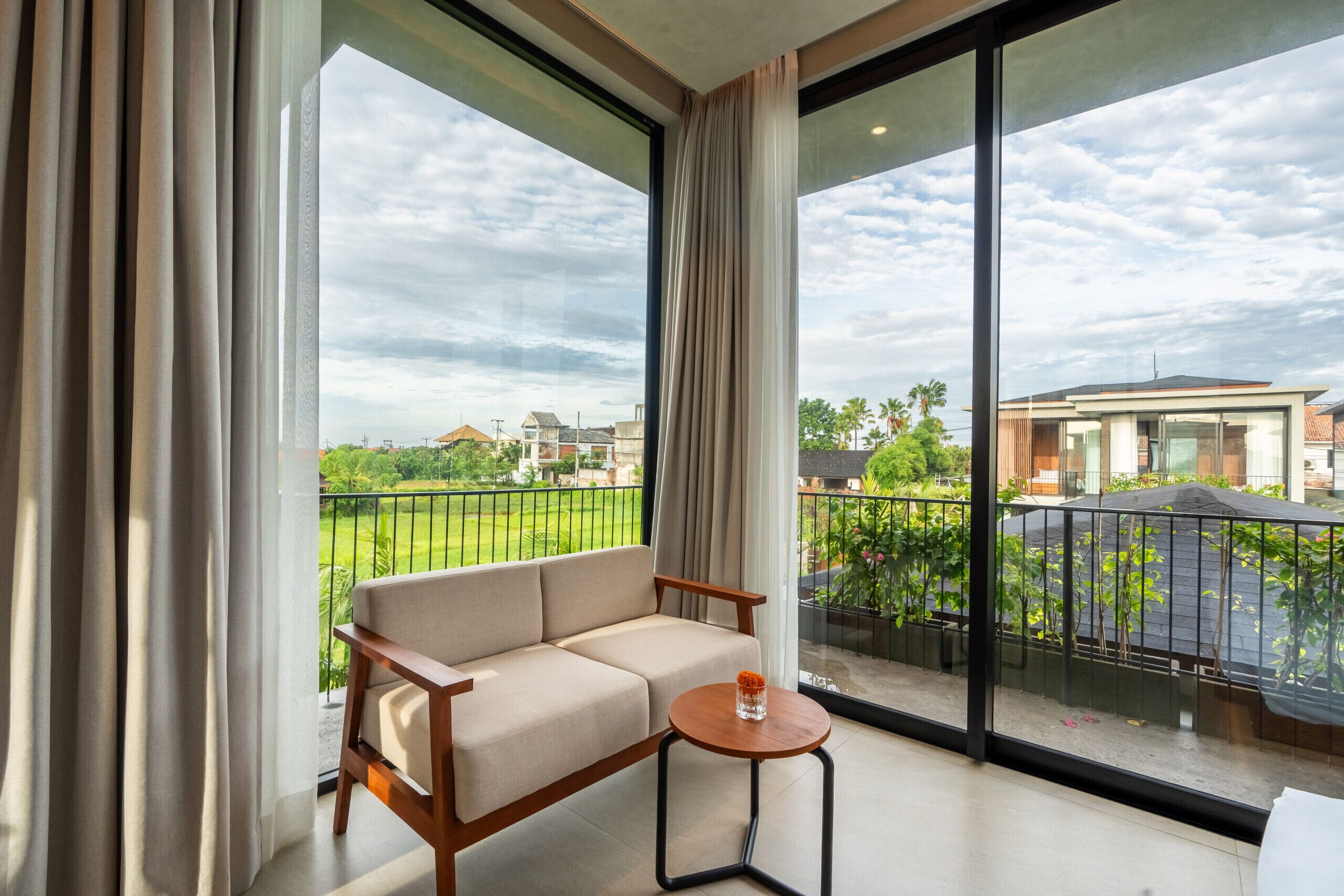 A balcony with a sofa and a small table, overlooking a green landscape and buildings.