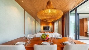 A modern dining room with a wooden table set for four, a large woven light fixture, and a television in the background. - 7BR Private Estate Near Berawa beach | 2 Pools (Kerobokan)