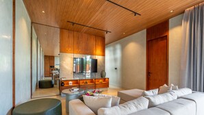 A modern living room with a wooden ceiling, a large flat-screen TV, a sofa set, and a coffee table with flowers. - 7BR Private Estate Near Berawa beach | 2 Pools (Kerobokan)