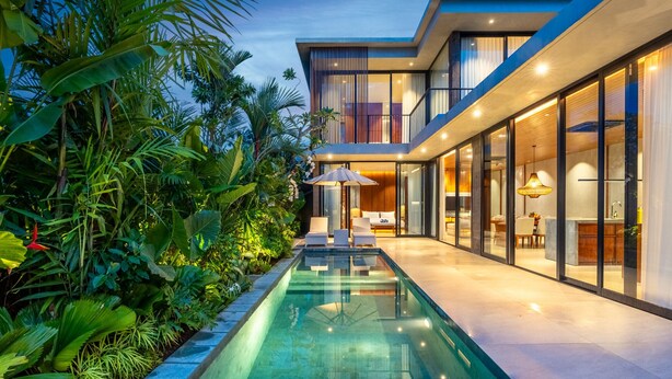 Una casa moderna con piscina, ampie vetrate e vegetazione lussureggiante.