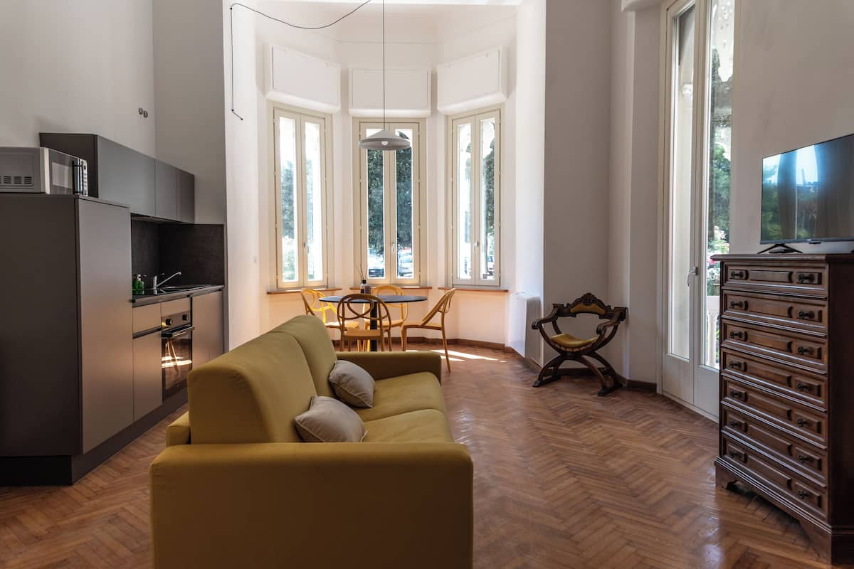 A modern kitchen with a built-in microwave, a dining area with a table and chairs, a sofa with cushions, and a wooden dresser with drawers.