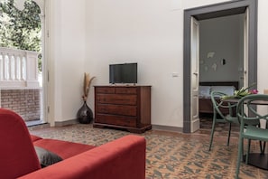 A room with a wooden dresser, a television on top, a red sofa, a dining table with chairs, and a patterned floor. - Villa Leda (Porto Recanati)