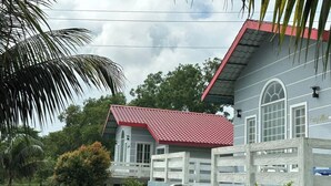 A two-story house with a red roof and white walls, surrounded by lush greenery and a wooden staircase leading to the entrance. - Hotel Rowshon Int Jamalpur (Jamalpur)