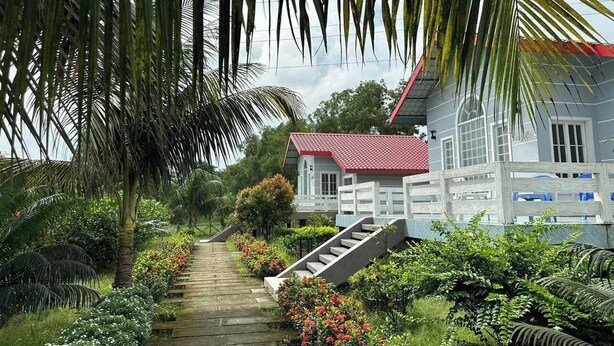 A pathway leading to a white building with a red roof, surrounded by lush greenery and flowering plants. - Hotel Rowshon Int Jamalpur (Jamalpur)