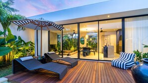 Een modern terras buiten met loungestoelen en een eethoek, omgeven door weelderige begroeiing.