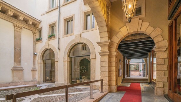 Een binnengang met stenen bogen, een rood tapijt en een bordje met 'Palazzo Monga'.