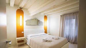 Een netjes opgemaakt slaapkamer met een groot bed, een nachtkastje, een spiegel en een raam met gordijnen.