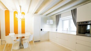 Een moderne keuken met witte kasten, een ingebouwde oven en een eethoek met een glazen tafel en witte stoelen.