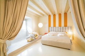 Un dormitorio con cama, mesita de noche, lámpara, ventana con cortinas y vista al cielo.