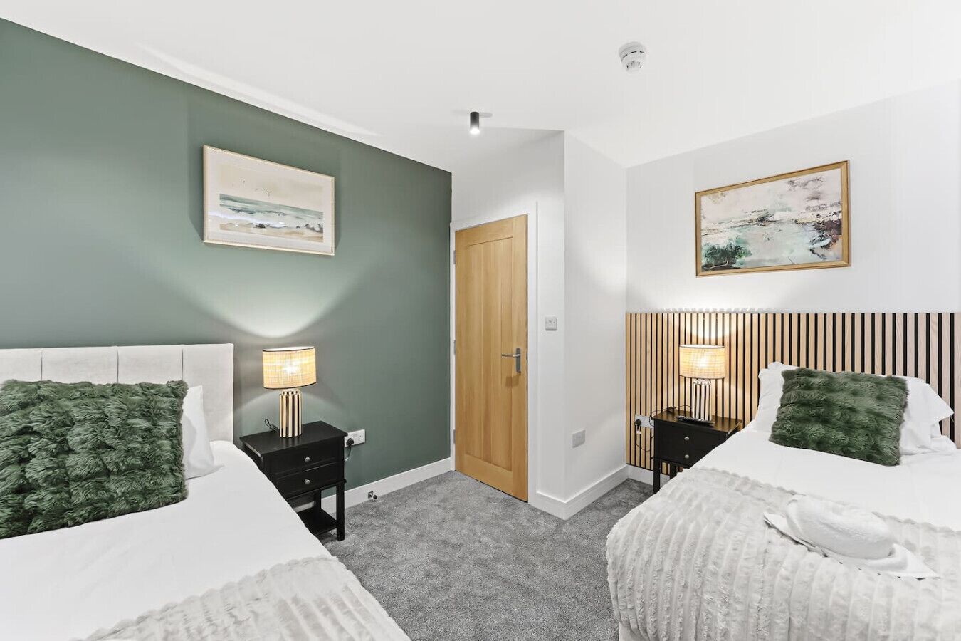 A hotel room with two beds, a wooden door, and a painting on the wall.