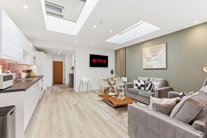 Eine moderne Wohnung mit Küche, Essbereich und Wohnzimmer. Ein Flachbildfernseher an der Wand zeigt 'NETFLIX'.