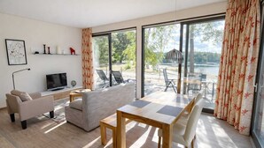 Ein modernes Wohnzimmer mit einer Couch, einem Fernseher, einem Holztisch und einem großen Fenster mit Seeblick.