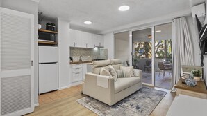 A modern kitchen with white cabinets, a built-in microwave, and a refrigerator. There is a beige sofa with pillows in the living area, and a wooden dining table with chairs. - Bright 1-Bed Apartment in Fortitude Valley (Fortitude Valley)