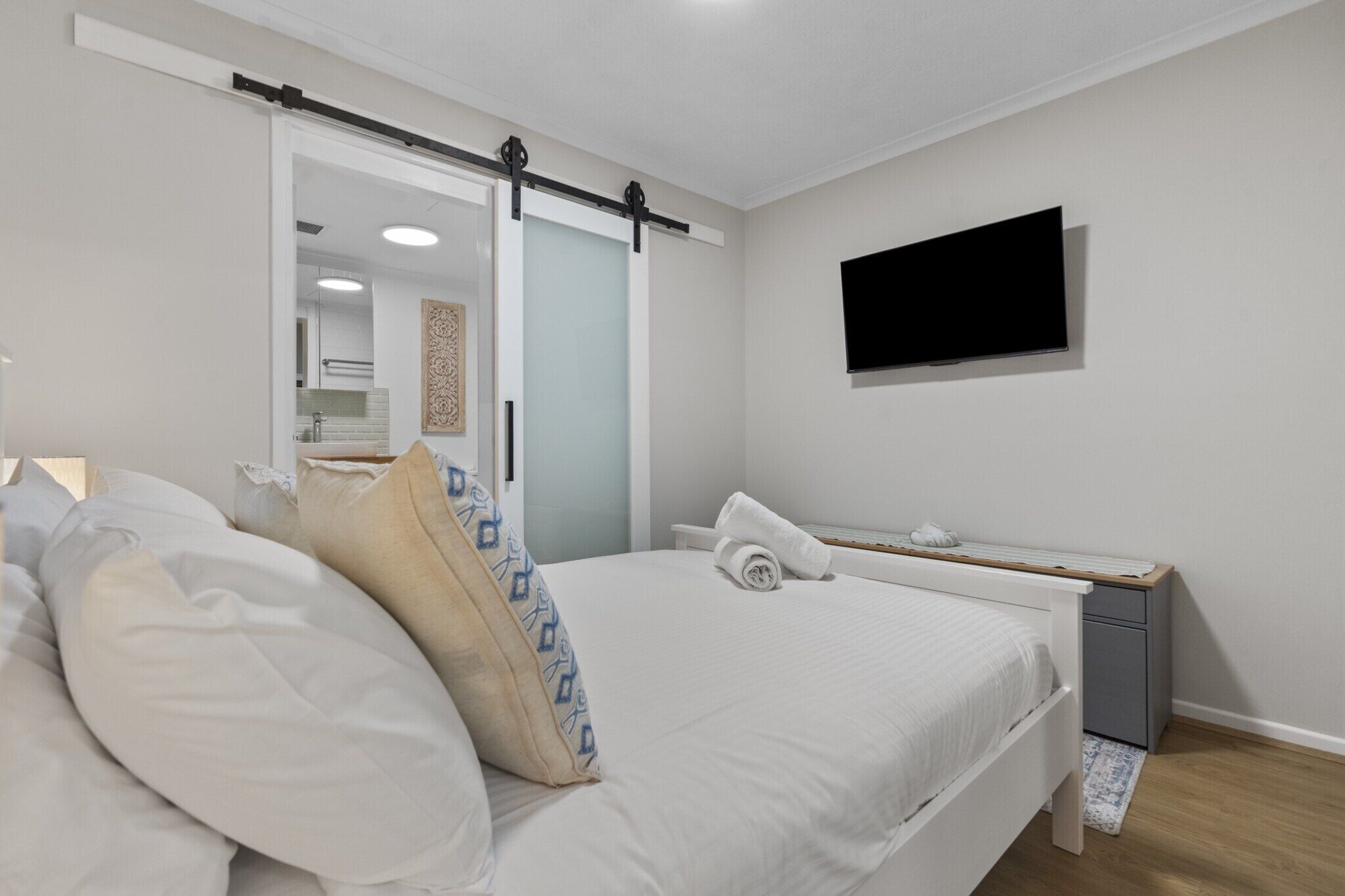 Un dormitorio con cama, escritorio, televisor y puerta corredera que da a un baño.