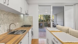 A modern kitchen with a wooden countertop, stainless steel sink, and white cabinets. There is a sliding door leading to an outdoor area with a chair and table. - Bright 1-Bed Apartment in Fortitude Valley (Fortitude Valley)